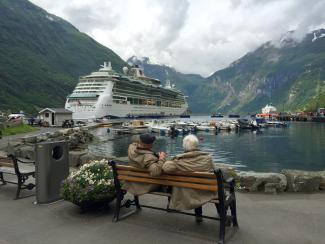 woman in brown coat sitting on brown wooden bench near white cruise ship during daytime by Julius Yls courtesy of Unsplash.