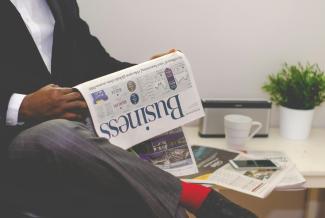 person sitting near table holding newspaper by Adeolu Eletu courtesy of Unsplash.